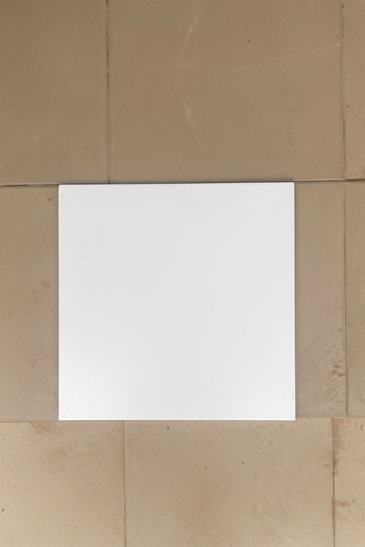 A plain white square tile or board centered on a tan tiled floor.
