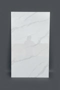 A large rectangular white porcelain tile with light gray marble-style veining, standing upright in a warehouse or showroom setting with cardboard boxes stacked in the background.