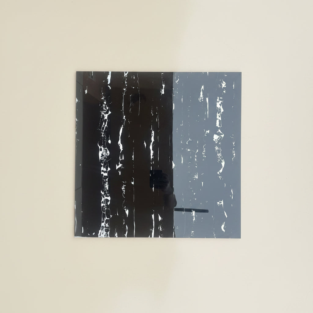 A square abstract wall art print or panel mounted on a plain beige wall. The artwork is split vertically into two textured sections: a very dark charcoal/black section on the left and a muted blue-gray section on the right, both with distressed white streaks.