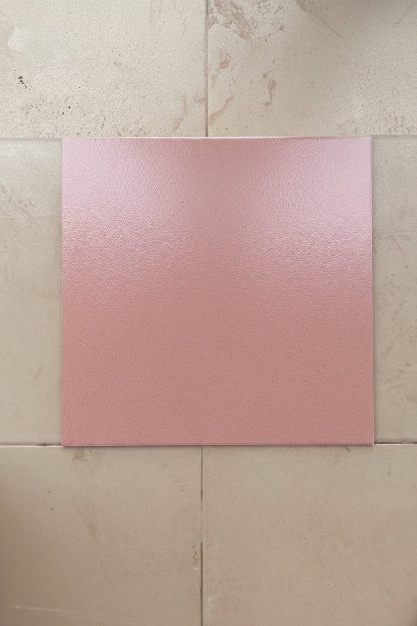 A square pink textured tile or sample card centered on a beige tiled surface.