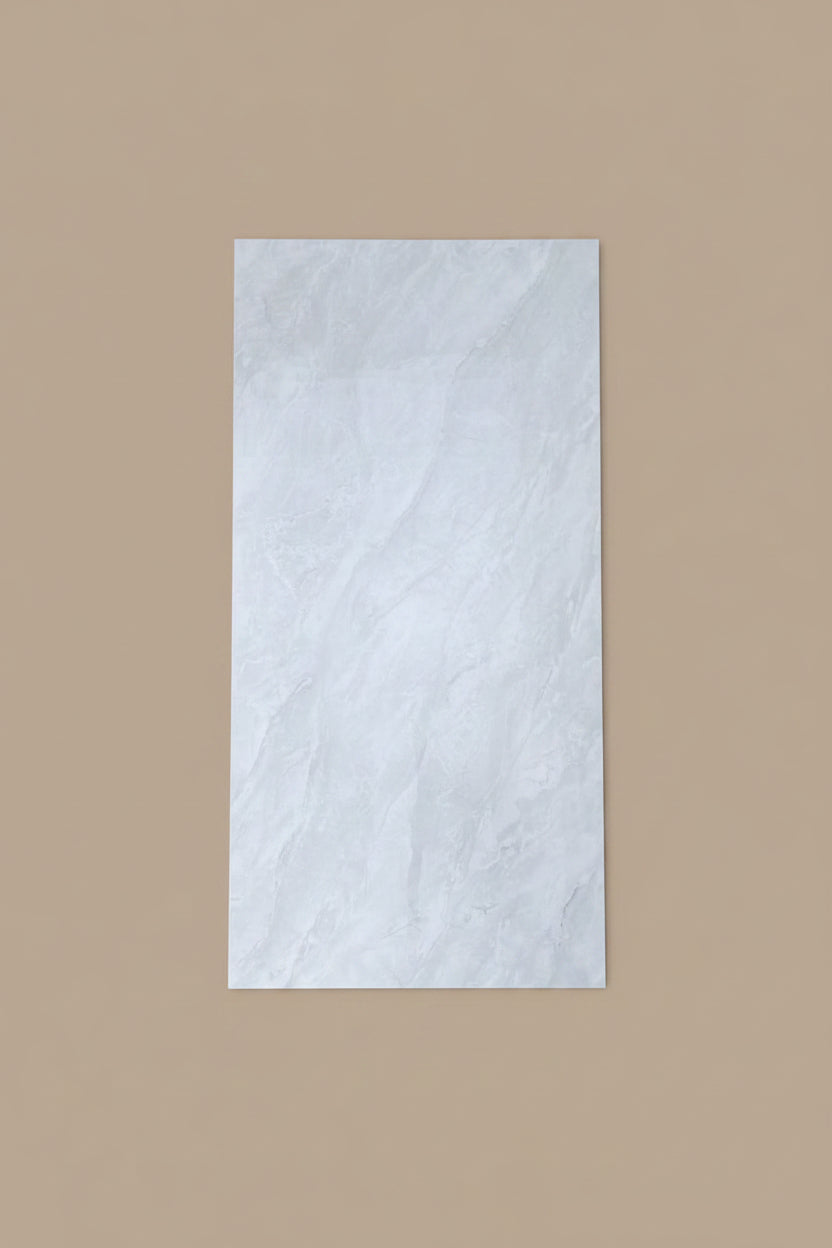 A large rectangular white marble-look tile or panel with subtle gray veining, shown standing on a beige tiled floor next to a person's legs in blue jeans and brown sandals.