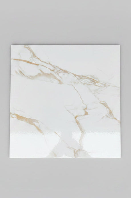 A single square white tile with light beige marble veining is placed on a larger beige tiled floor. A person's feet wearing brown sandals and blue jeans are visible at the bottom edge of the frame.